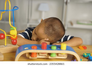 Niño durmiendo sobre la mesa dentro de la casa después de jugar con juguetes. Foto de stock