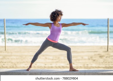 Musta nainen, afro kampaus, joogaa soturi poseeraa rannalla. Nuori Nainen yllään urheilu vaatteita meri taustalla Arkistovalokuva