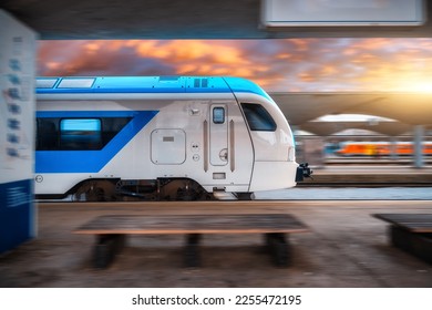 日没時に鉄道駅で動いている青の高速列車。高速な近代的な都市間電車とぼかした背景。プラットホームスロベニアの鉄道。商業および旅客輸送の写真素材