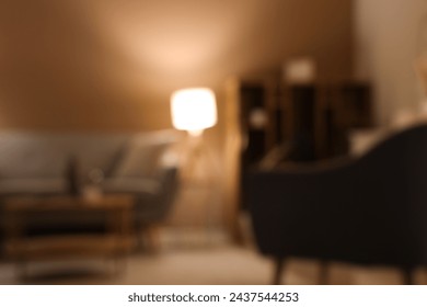 灰色のソファ、肘掛け椅子、夕方の輝くランプが付いたモダンなリビングルームのぼやけた景色の写真素材