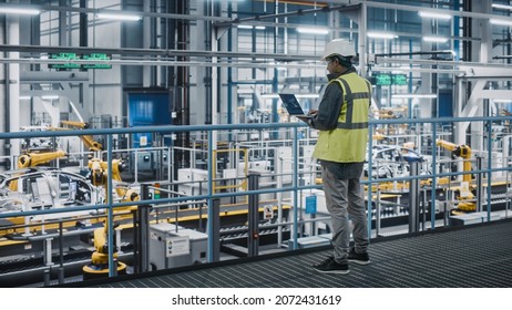 Car Factory Engineer in High Visibility Vest Using Laptop Computer. Automotive Industrial Manufacturing Facility Working on Vehicle Production with Robotic Arms Technology. Automated Assembly Plant. Stockfoto