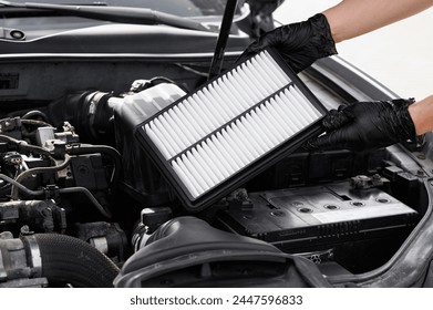 Car mechanic holds car air filter in hands near engine compartment, plans to replace old filter, close-up. Concept replacing auto parts, car maintenance, protection from allergens, dirt, soot. 库存照片