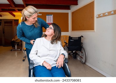 Caregiver pushing the wheelchair of a disabled woman in a day center for people with special needs 库存照片