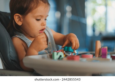 自宅でテーブルの上に座って数学パズルゲームで遊ぶ白人の少女。早期開発のコンセプト。木のカラフルなスタッキングと仕分けおもちゃ子の写真素材