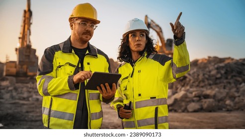 Стоковая фотография: Caucasian Male Civil Engineer Talking To Hispanic Female Inspector And Using Tablet Computer On Construction Site of New Building. Real Estate Developers Discussing Business, Excavators Working.
