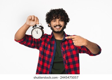 Cheerful young Indian man in casual clothes showing time on clock isolated over white background. Hindi boy having deadline, checking on time, hurrying up Foto stock