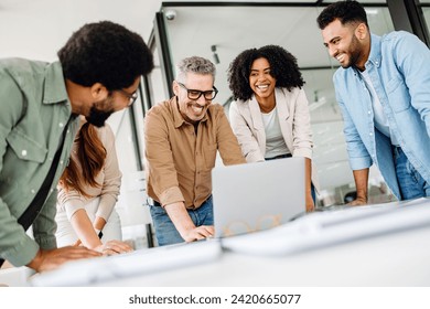 A cheerful group of diverse coworkers lean in around a laptop, indicative of an interactive tech discussion and the high spirits characteristic of a productive and forward-thinking team. Foto stock