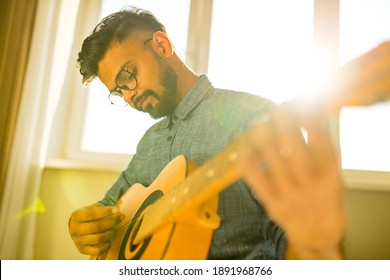 Cheerful handsome young man playing guitar and smiling in new cozy apartment Stockfotó
