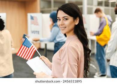 Mujer asiática alegre y feliz, ciudadana estadounidense sosteniendo bandera estadounidense y cédula de votación parada en fila para votar, eligiendo candidato en centro de votación. Concepto de democracia, voto Foto de stock