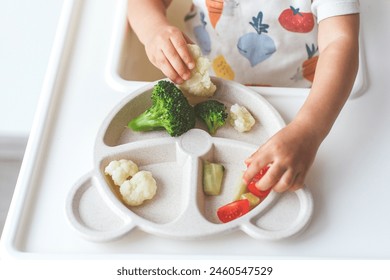 children's plastic plate with vegetables broccoli, cauliflower, cucumbers, tomatoes, child eats. Foto stock