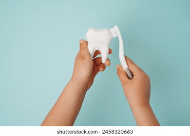 Child's hands holding white tooth and toothbrush on blue background. Healthy care teeth concept 库存照片