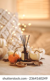 Concept of cozy fall home atmosphere, aromatherapy. Perfume, appartment aroma diffuser with autumn scent of pumpkin spicy latte, cinnamon, anise. Room decor with pumpkins, dry orange, wool plaid Foto Stock