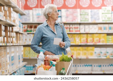Anciana confundida comprando comestibles en el supermercado, sostiene una lista de compras y mira alrededor Foto de stock