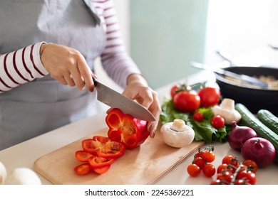 料理のコンセプト。グレイのエプロンを着た目立たない女性が健康的なディナーを作り、家でおいしい食事を準備する女性の切り取り、まな板の上で野菜を切り、キッチンのインテリア、接写の写真素材