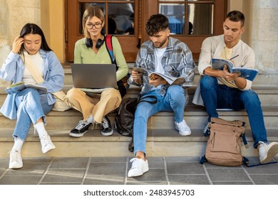 College students with books studying on laptop sitting on staircase of college campus 庫存照片