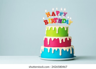 カラフルな誕生日キャンドルとドリップアイシングを備えたカラフルなティアードバースデーケーキの写真素材