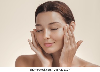 Cosmetics skincare concept photo. Woman with beautiful face touching healthy facial skin portrait. Beautiful smiling Asian girl model with natural makeup enjoys glowing hydrated smooth skin on beige 库存照片