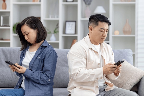 Couple sitting apart on a sofa, focusing on their smartphones. Concept of technology affecting relationships and communication. Foto stock