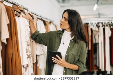 信頼できるタブレットの助けを借りて、在庫を指揮する衣料品店の所有者は彼女の店で取り込みます。在庫が正確で最新であることを確認するためのアイテムの確認とカウントに焦点を当てたビジネスマンの写真素材