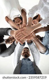 Close up view from below of excited multiracial businesspeople stack hands in pile motivated for shared victory, happy multiethnic colleagues engaged in teambuilding activity, show team unity Stock fotografie