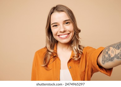 Joven mujer feliz sonriente que usa camisa naranja ropa casual haciendo selfie shot pov en el teléfono móvil aislado en liso pastel luz beige fondo estudio retrato. Concepto de estilo de vida Foto de stock