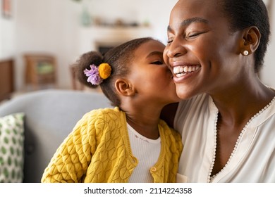 Close up of beautiful daughter kissing mother on cheek at home. African little girl giving kiss to happy mother. Lovely black female child kissing cheerful and proud woman on cheek for mother's day. Stock Photo