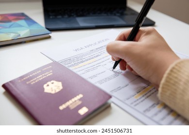 Primer plano de la mano femenina rellenando un documento de solicitud de visa con un pasaporte alemán, fondo borroso  Foto de stock