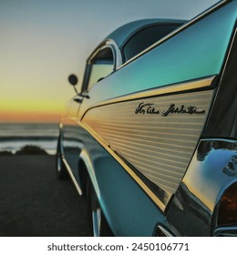 Close up photo of dramatic  highly photorealistic outdoor closeup of a 1957 light blue, highly reflective chevy hot rod at sunset with the ocean and beach in the background. depth of field
