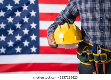 Close up shot of labour with tools or equipment by holding helmet in hand in front of USA flag - concept of maintence service, labour day and employment. Stock Photo