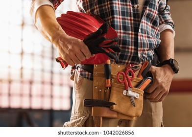 ハードハットと建設機器を持つレンガ職人の手の接写。作業用手袋を持ち、ツールキットを腰に装着したメイソン男性の詳細。工具ベルトと職人用の機材を持つハンディマン。の写真素材