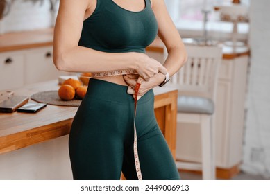 밝은 주방에서 테이프와 함께 허리를 측정 스포티 한 여자의 자른된 보기. 체중 감량 및 식이 개념  스톡 사진