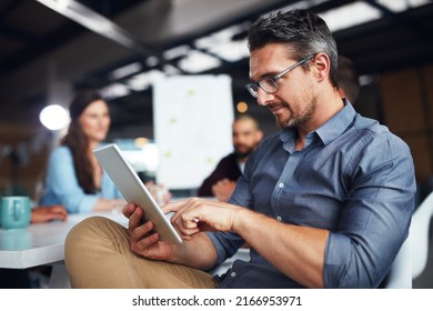 制作プロセス。オフィスのテーブルに座った男性がデジタルタブレットを使ってバックグラウンドで作業している同僚のショット。の写真素材