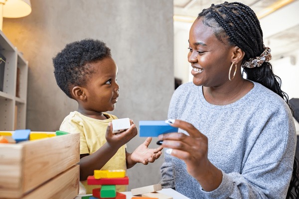 Un lindo niño africano juega con coloridos juguetes didácticos educativos. Su orgullosa madre lo apoya. Profesora de guardería con niño. Foto de stock