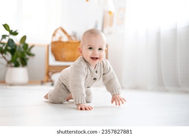 lindo niñito con traje de punto de lana pastel aprendiendo a arrastrarse en el suelo en una sala de estar brillante, sonriente bebé, jugando, desarrollo temprano de niños Foto de stock