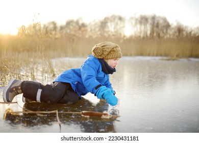 寒く晴れた冬の夕暮れ時に、凍った湖や川の氷の上に可愛い未就学児が落ちた。冬の子供の屋外ゲームの危険性の写真素材