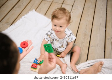 Niño lindo jugando con coloridos juguetes educativos en una cubierta de madera, centrándose intensamente en las piezas. Fomentar el aprendizaje y el desarrollo tempranos. Foto de stock