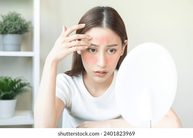 Dermatology, scratch asian young woman looking at mirror, expression worry and itch, itchy allergy or allergic sensitive reaction, red spot or rash on her face. Beauty care from skin problem treatment Stockfotó