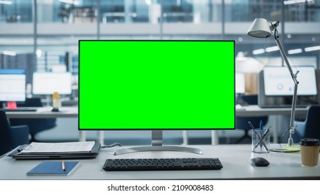 Desktop Computer Monitor with Mock Up Green Screen Chroma Key Display Standing on the Desk in the Modern Business Office. In the Background Glass Wall with Big City Office. Stockfoto