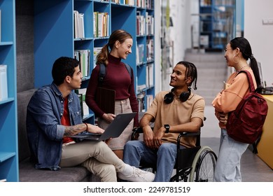 大学の図書館で元気にチャット車椅子の若い男性と学生の多様なグループ、包摂性のコンセプトの写真素材