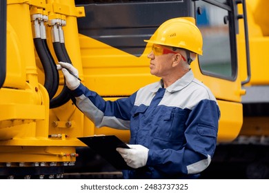 Le mécanicien du conducteur vérifie les tuyaux hydrauliques de la pelle. Un homme en dur labeur industriel. : photo de stock