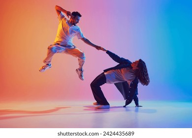 Dynamic photo of man leaping, woman bending backwards against vivid pink-blue gradient background. Energetic dance pose. Concept of youth culture, music, style, fashion, action. Gel portrait. Foto stock