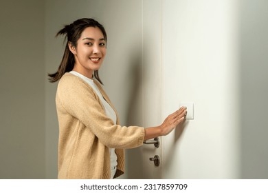 Earth Hour. Asian beautiful woman turn off or on the light to saving electrical energy. Finger pushing light switch turn on or off. White switch Arkistovalokuva