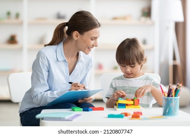 Desarrollo infantil temprano. Un niño lindo jugando a un juego de geometría lógica, una mujer positiva especialista con notas observándolo en la oficina Foto de stock