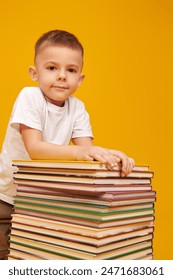Educación y desarrollo temprano de los niños. Retrato de un niño pequeño inteligente abrazando una pila de libros. Fondo de estudio amarillo.   Foto de stock