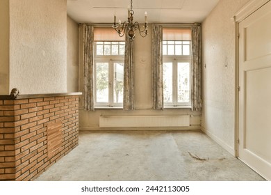 An empty room with sunlight streaming through large windows, adorned with a vintage chandelier and a brick fireplace, waiting to be furnished. 库存照片