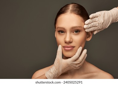 estheticians in medical gloves examining face of woman on grey background, dermatology concept Stockfotó