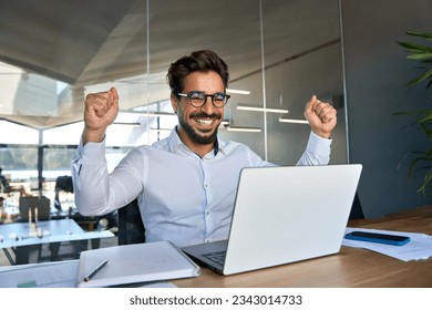 Excited professional young Latin business man celebrating success raising fist happy about financial bank market growth or reward work results, corporate goals achievement looking at laptop in office. – Ảnh có sẵn