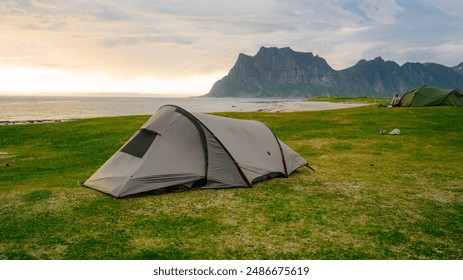 Experience the tranquility of camping by the Norwegian coast. This scenic view features a tent set up on lush green grass with the breathtaking backdrop of mountains and the sea. Ideal for outdoor 库存照片