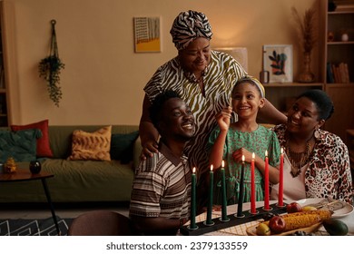 Family letting little girl to light colorful candles for Kwanzaa celebration: stockfoto