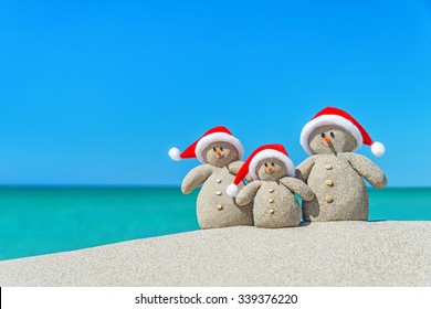 Family of Snowmen in santa hats at tropical beach. New Year's and Christmas holiday in hot countries concept. Stock Photo